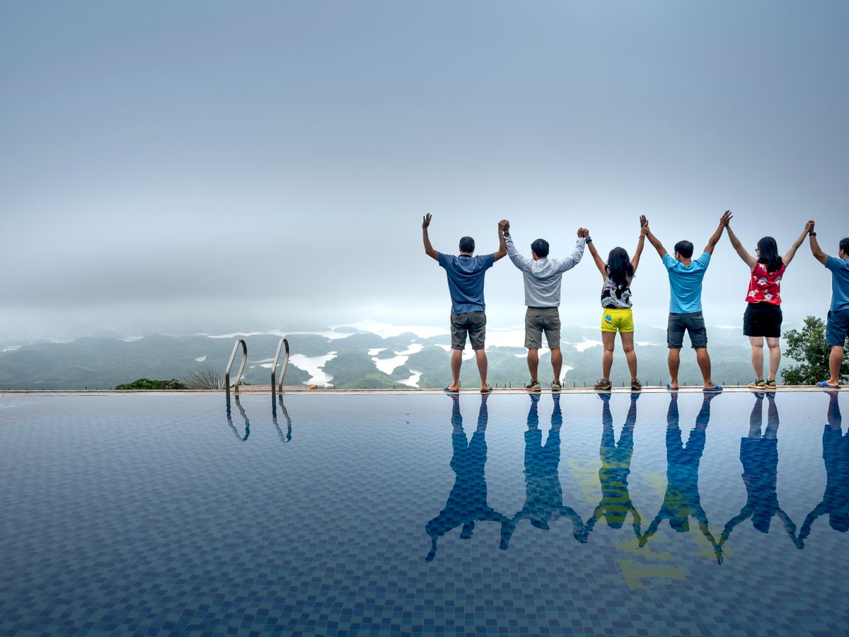 A team on a company offsite raising joined hands beside an infinity pool overlooking a lake landscape