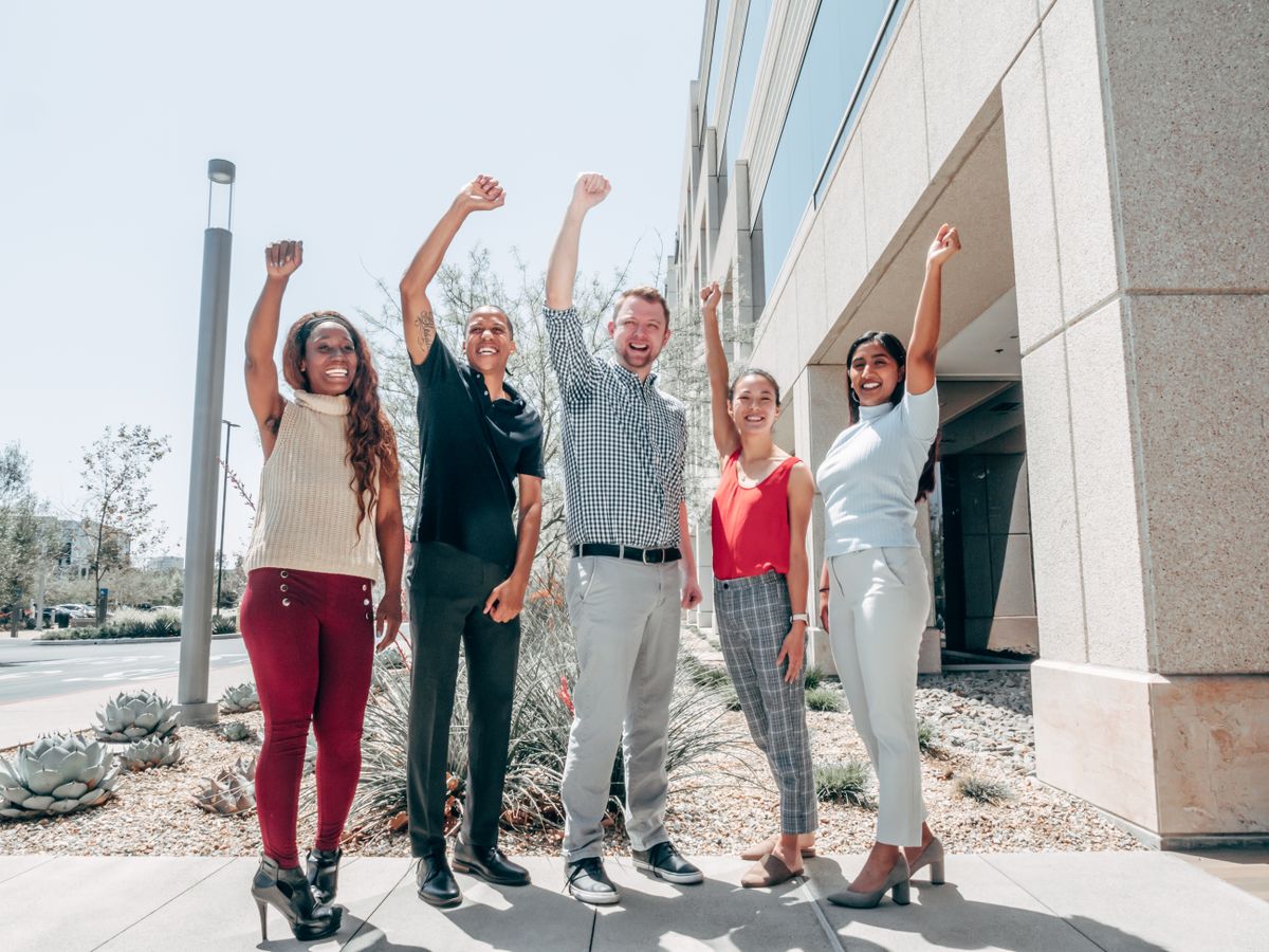 A team of colleagues in office attire cheering together outside their company building